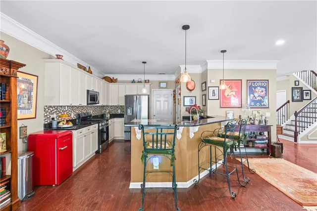 a open kitchen with stainless steel appliances granite countertop a stove top oven a refrigerator a dining table chairs and couches with wooden floor