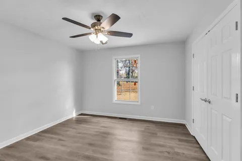 an empty room with wooden floor chandelier fan and windows