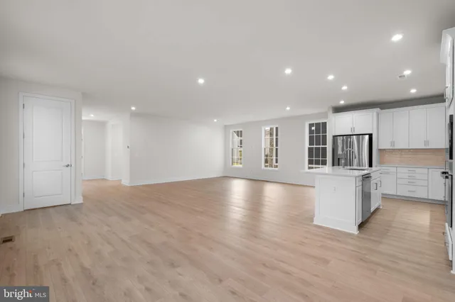 a view of empty room with wooden floor and kitchen