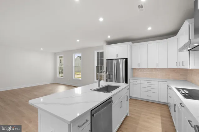 a kitchen with stainless steel appliances granite countertop a sink a stove a refrigerator and white cabinets with wooden floor