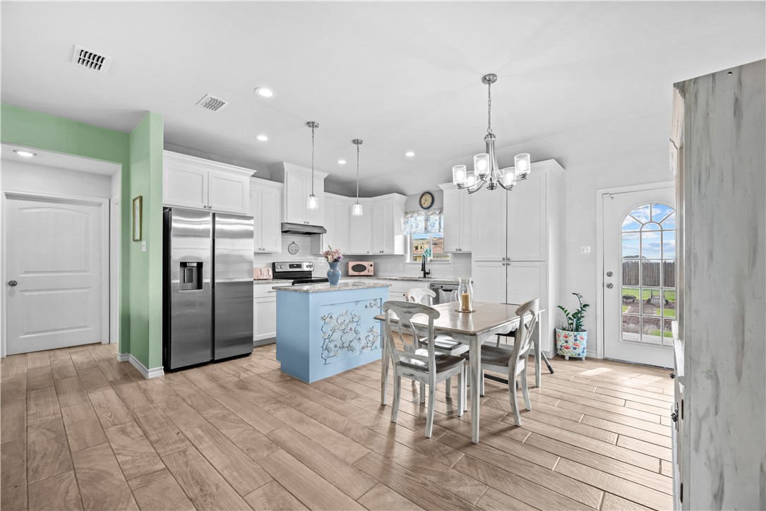 103 Atkinson Drive Orange Grove, TX 78372 - Photo 12 of 30 a kitchen with stainless steel appliances kitchen island granite countertop a refrigerator a stove a dining table and chairs with wooden floor