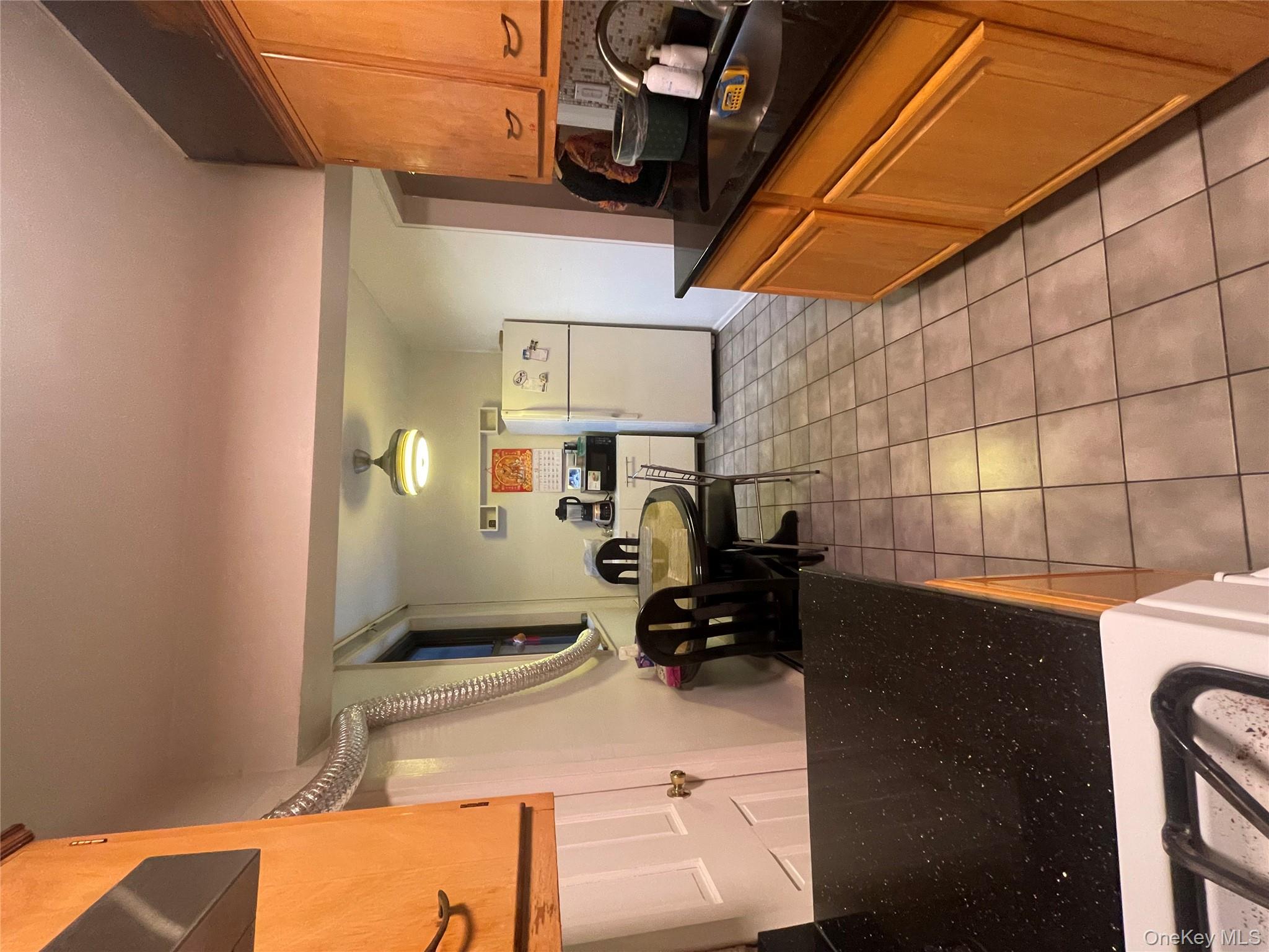 99-35 59th Avenue, Unit 5E Queens, NY 11368 - Photo 7 of 11 Kitchen with fridge, light tile patterned floors, brown cabinetry, dark stone counters, and range