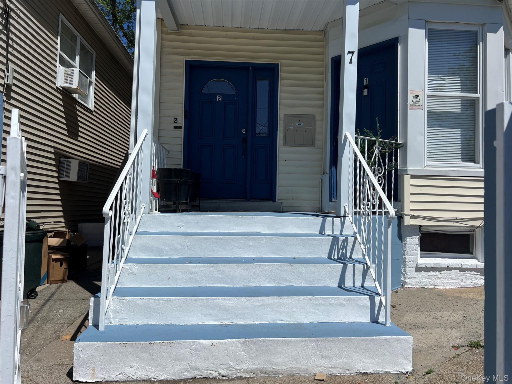 7 Clinton Street Haverstraw, NY 10927 - Photo 2 of 20 Property exterior featuring cream-colored siding, a prominent orange-painted concrete staircase, and two blue entry doors