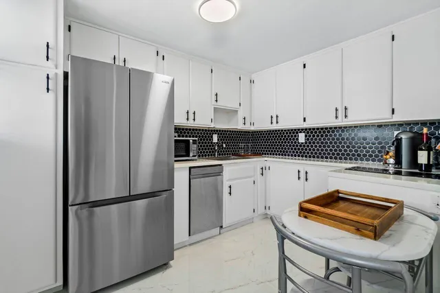 a kitchen with stainless steel appliances granite countertop a refrigerator a sink a stove and white cabinets