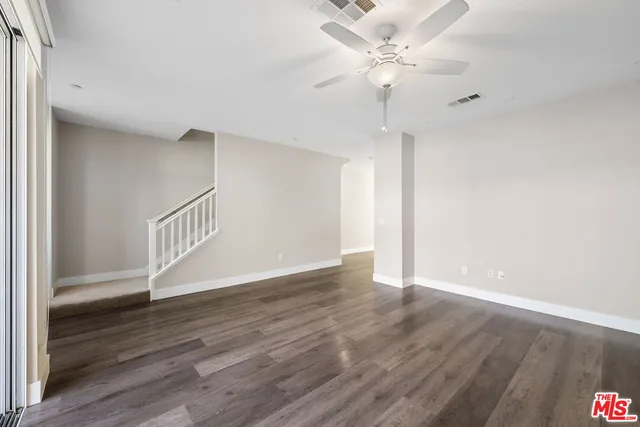 a view of an empty room with wooden floor and a ceiling fan