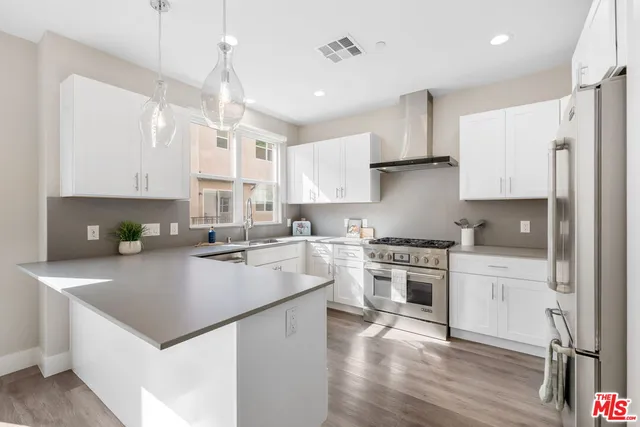 a kitchen with a stove a sink dishwasher a refrigerator and white cabinets with wooden floor