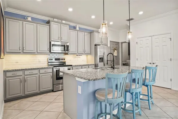 a kitchen with stainless steel appliances granite countertop a sink a stove a refrigerator and chairs