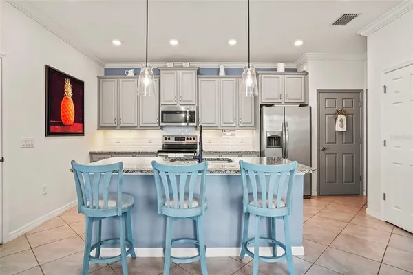 a kitchen with stainless steel appliances kitchen island granite countertop a dining table chairs and a refrigerator