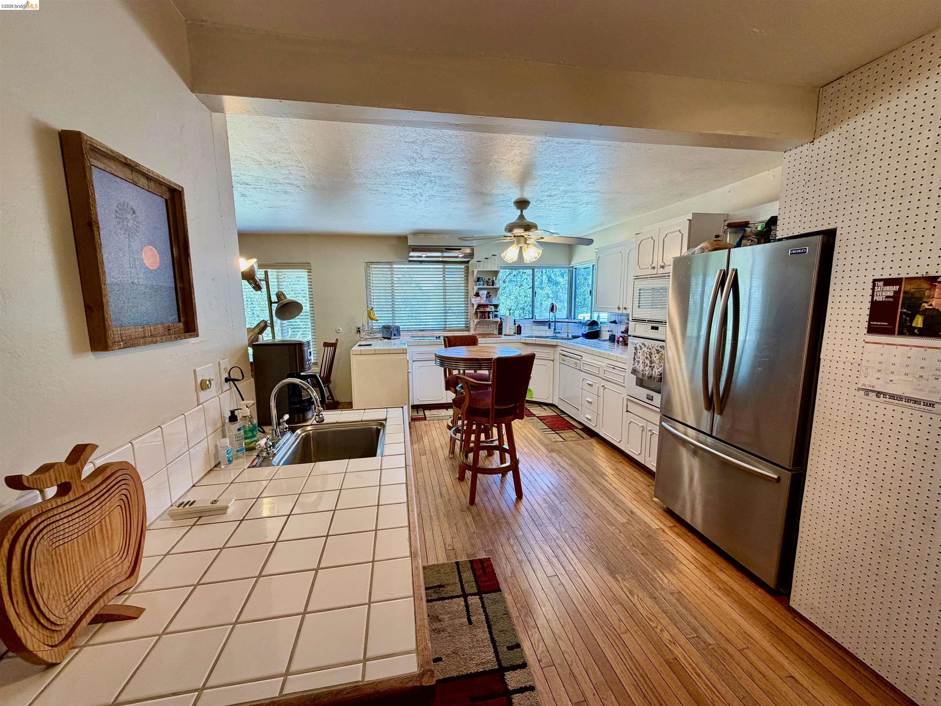 18195 Wards Ferry Road Sonora, CA 95370 - Photo 64 of 67 Open-concept kitchen featuring wood-finish flooring, white cabinetry, stainless steel appliances, a ceiling fan, and tile countertops with a sink