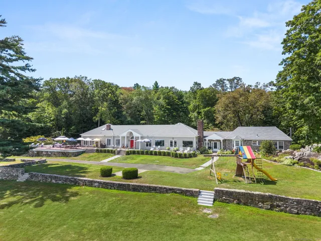 a view of a swimming pool with lawn chairs and large trees