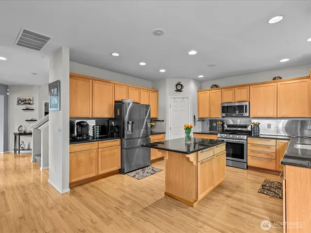 a kitchen with stainless steel appliances granite countertop a refrigerator a stove top oven a sink and dishwasher with wooden floor