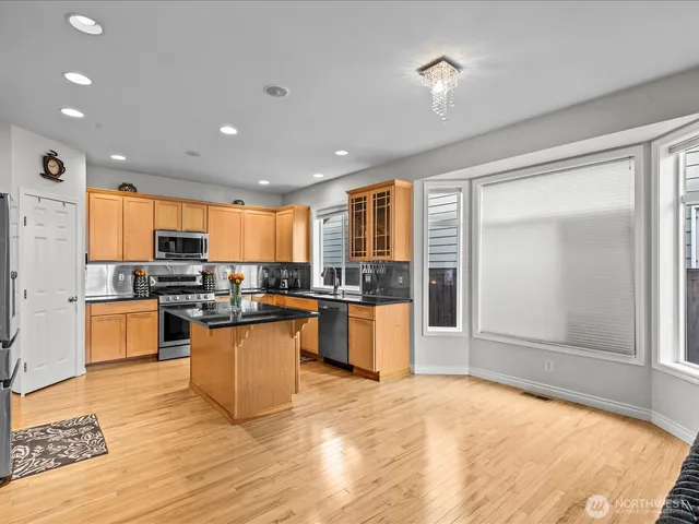 a open kitchen with granite countertop a refrigerator oven a sink dishwasher and white cabinets with wooden floor