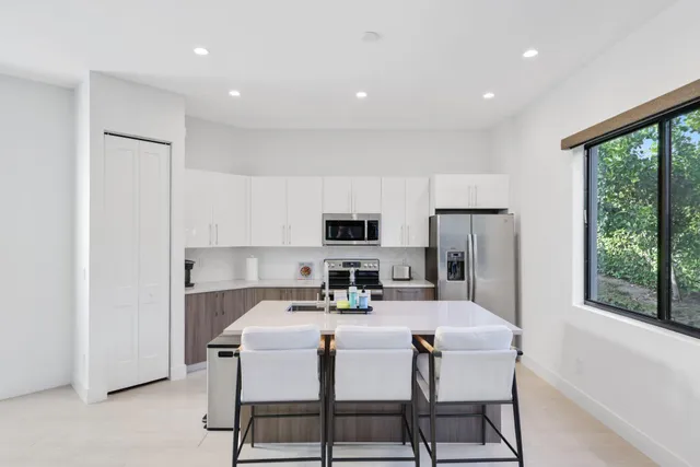 a kitchen with stainless steel appliances a stove a sink a refrigerator cabinets and a dining table with large windows