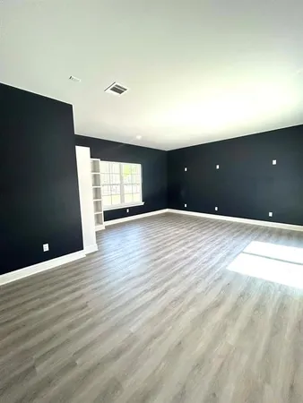a view of an empty room with wooden floor and a kitchen