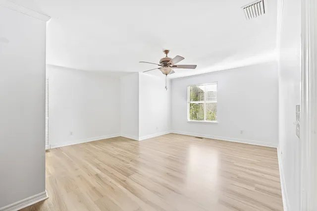 an empty room with wooden floor chandelier fan and windows
