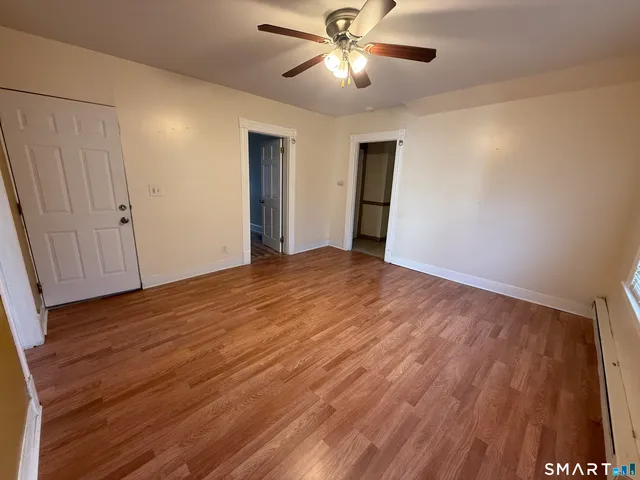 a view of an empty room with wooden floor and a ceiling fan