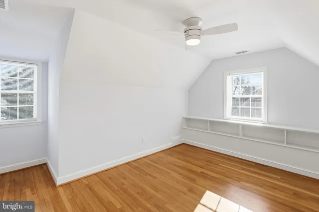 an empty room with wooden floor fan and windows