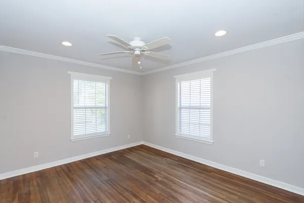 an empty room with wooden floor ceiling fan and windows