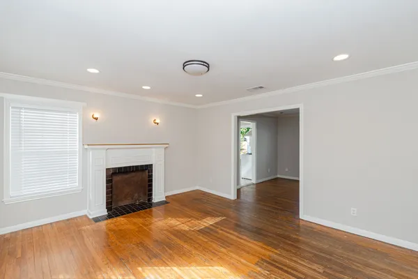 a view of an empty room with wooden floor fireplace and a window