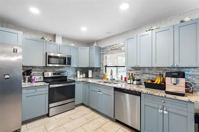 a kitchen with stainless steel appliances granite countertop a sink dishwasher a refrigerator and white cabinets with wooden floor
