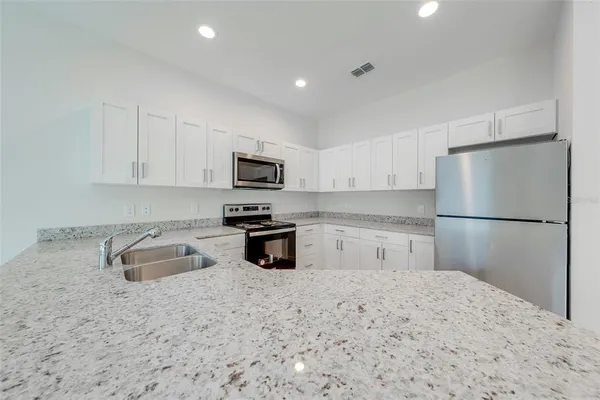 a kitchen with granite countertop a refrigerator sink stove and white cabinets