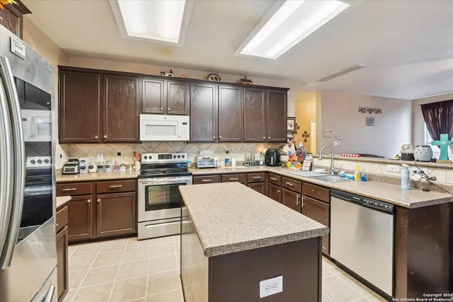 a kitchen with stainless steel appliances granite countertop a refrigerator a sink dishwasher a stove and white countertops with wooden floor