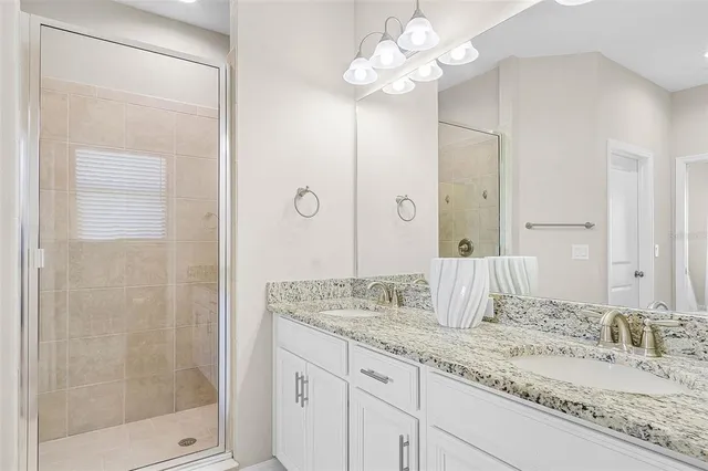 a bathroom with a granite countertop double vanity sink a mirror and shower