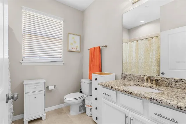 a bathroom with a granite countertop toilet a sink a mirror and a window