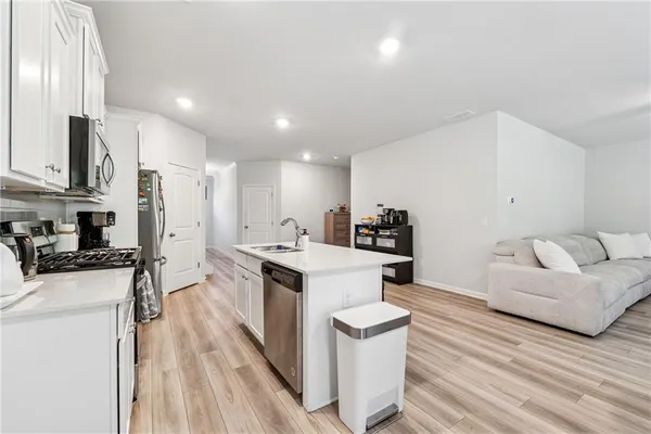 a kitchen with stainless steel appliances kitchen island granite countertop a stove a sink a refrigerator and white cabinets with wooden floor