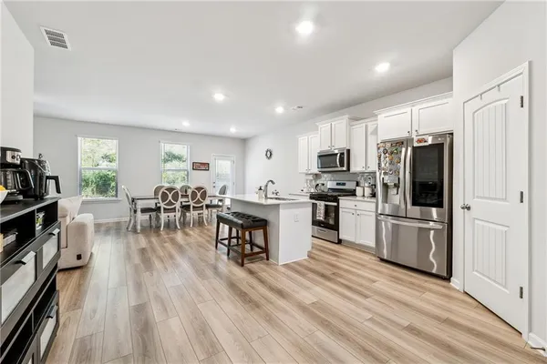 a kitchen with stainless steel appliances a refrigerator a stove top oven a dining table and chairs with wooden floor