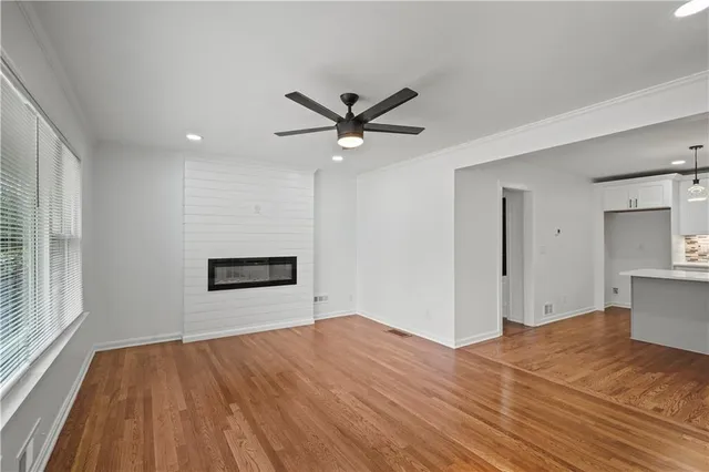 a view of empty room with wooden floor and kitchen view
