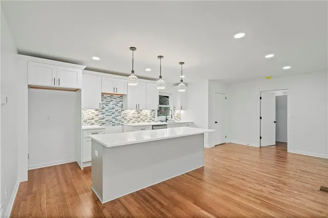 a large kitchen with stainless steel appliances a large counter top a sink dishwasher and a refrigerator with wooden floor