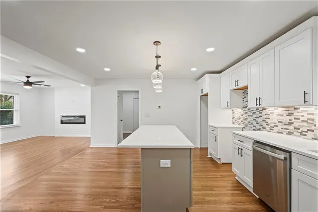 a kitchen with stainless steel appliances kitchen island granite countertop a refrigerator a sink dishwasher and white cabinets with wooden floor