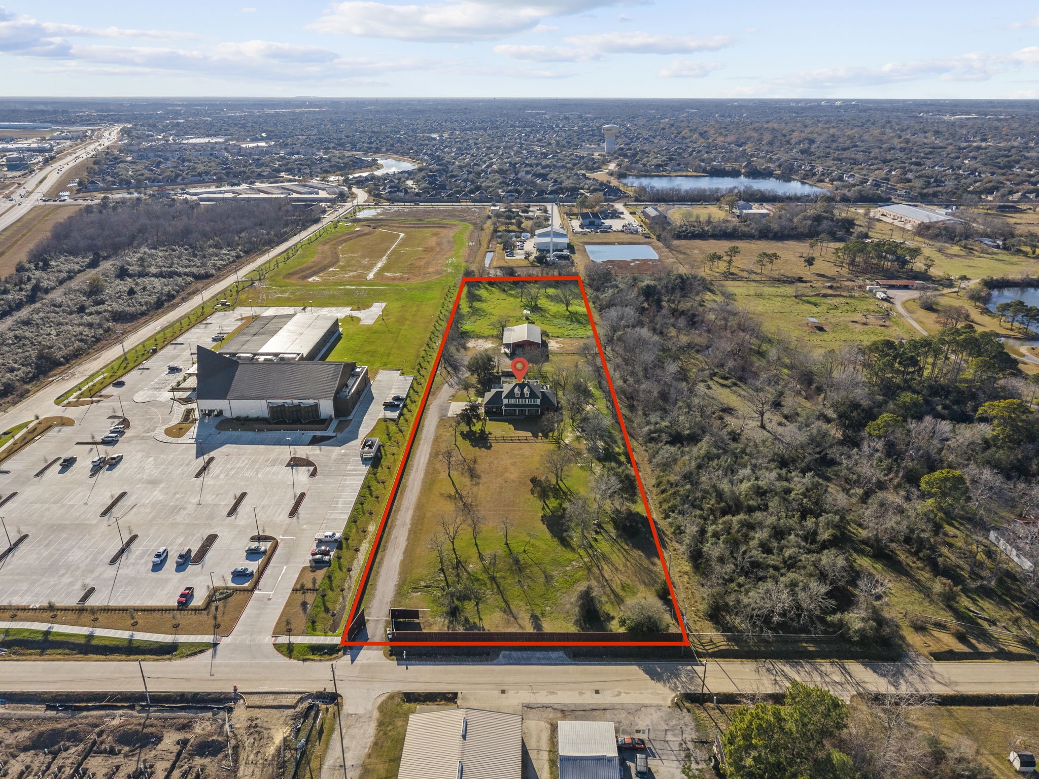 2730 Lawrence Road Kemah, TX 77565 - Photo 45 of 46 This aerial photo shows a long, rectangular property outlined in red, featuring a house surrounded by open land and trees. It's located near a large building with a parking lot and is set in a semi-urban area with nearby roads and other structures.