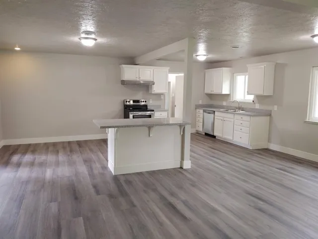 a kitchen with stainless steel appliances granite countertop a stove a sink and white cabinets with wooden floor