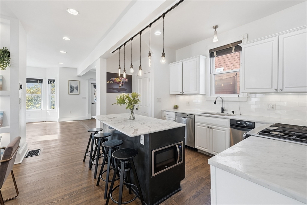 22 Spring Street Everett, MA 02149 - Photo 11 of 40 a kitchen with stainless steel appliances kitchen island a table chairs in it white cabinets and a wooden floor