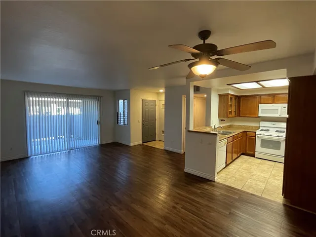 a view of an empty room and kitchen with wooden floor