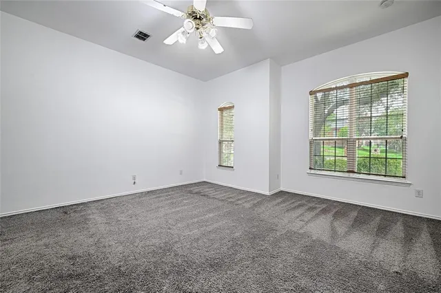 an empty room with chandelier fan and windows