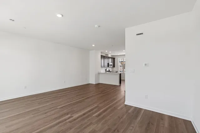 a view of kitchen and empty room with wooden floor