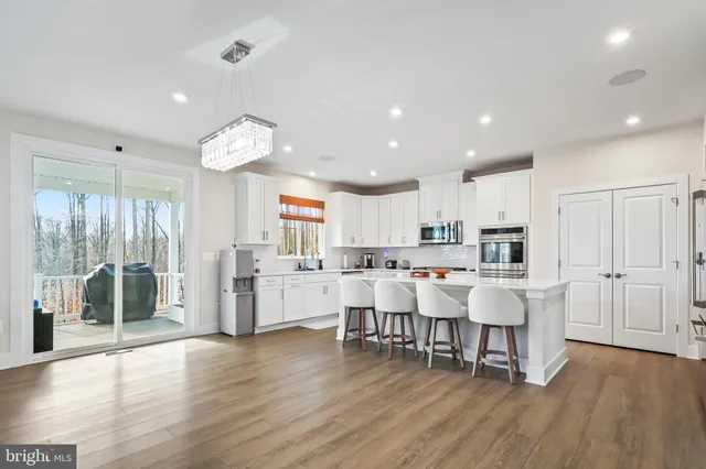 a large white dining hall with stainless steel appliances granite countertop a stove oven a dining table and chairs with wooden floor