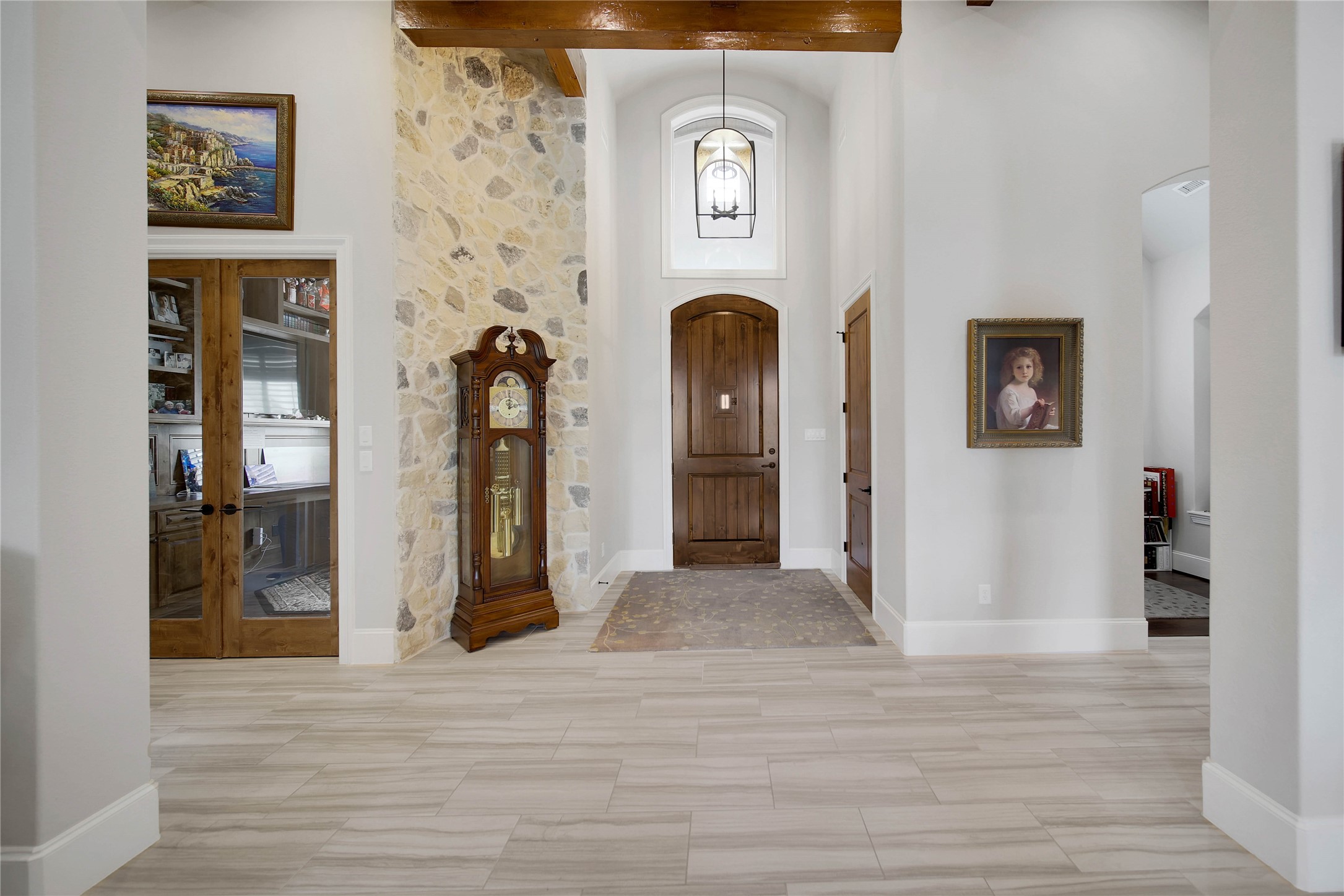 Elegant entryway featuring a grand wooden door, stone accent wall with a classic grandfather clock, and beautifully tiled flooring.
