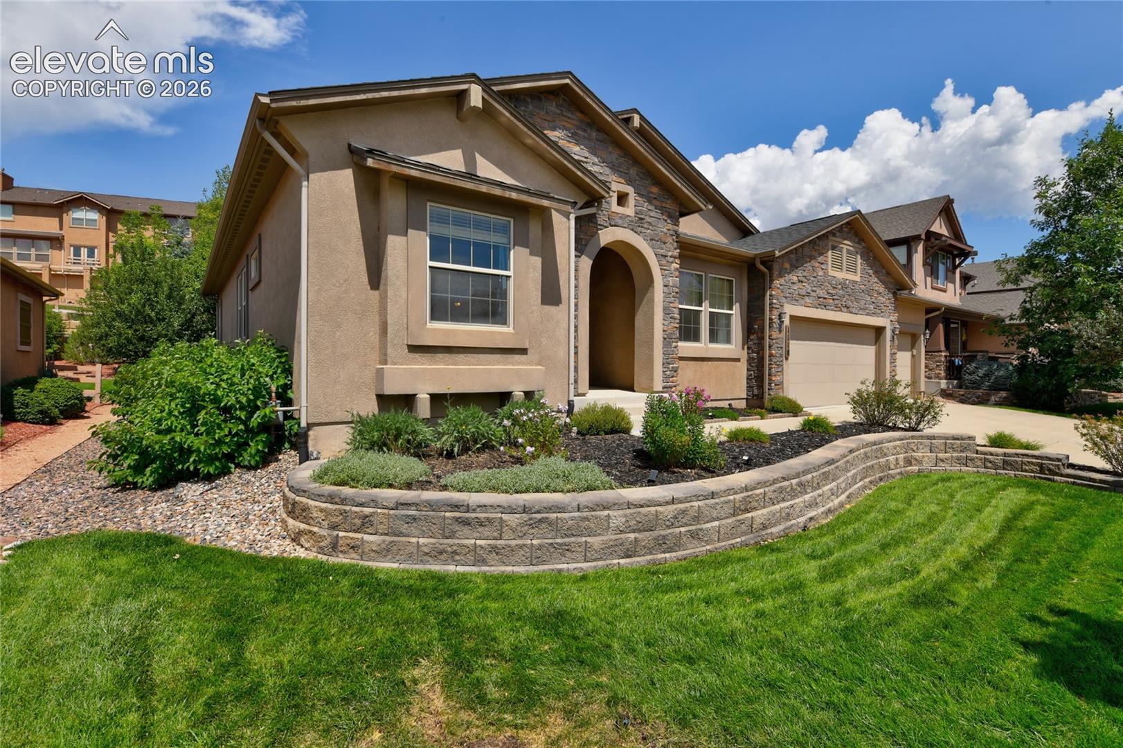 1118 Spectrum Loop Colorado Springs, CO 80921 - Photo 3 of 50 Stone and stucco exterior, arched entry, two-car garage, front yard with retaining wall, and landscaped planting beds