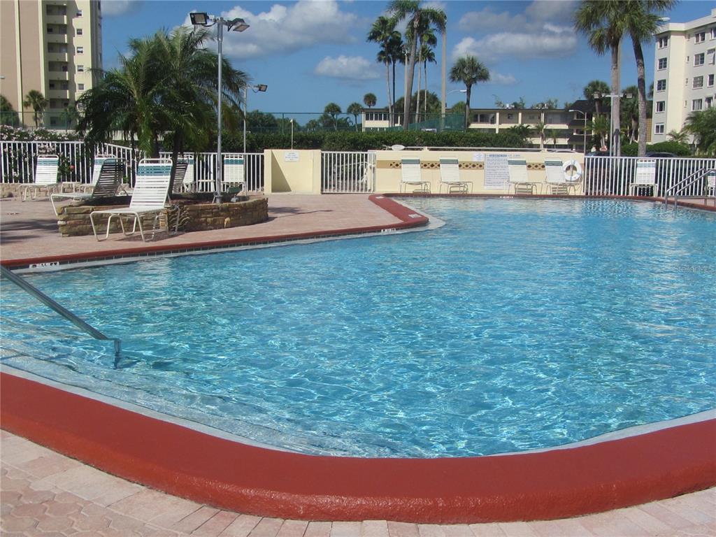 4775 Cove Circle, Unit 1202 Madeira Beach, FL 33708 - Photo 25 of 32 a view of a swimming pool with a lawn chairs and palm tree