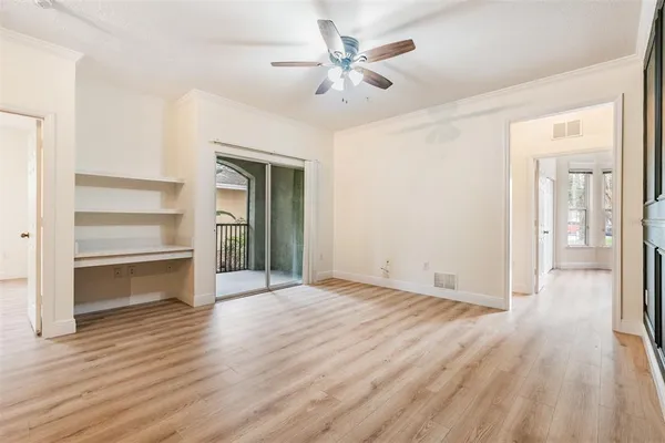 an empty room with wooden floor fan and windows