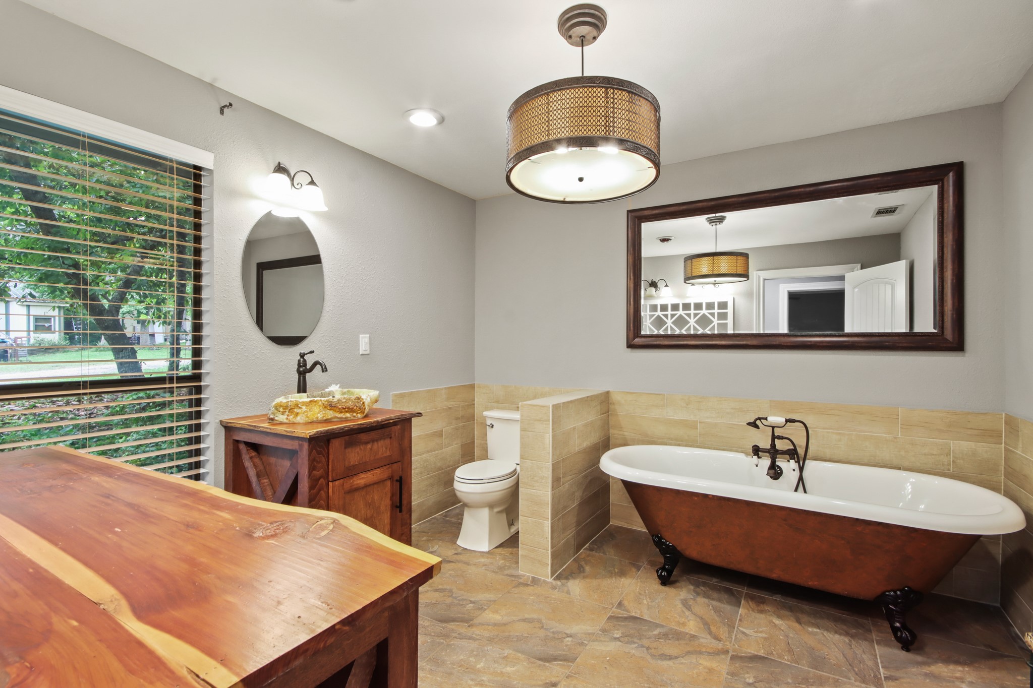 35 Susan Drive Cleveland, TX 77327 - Photo 15 of 33 This bathroom features a rustic design with a freestanding clawfoot tub, wooden vanity with a stone sink, and large wall-mounted mirror. It has a window with blinds, tiled flooring, and modern lighting for a cozy, elegant feel.