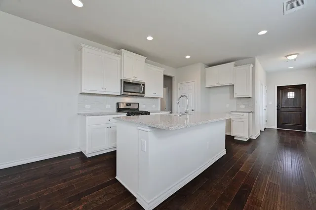 a kitchen with stainless steel appliances a refrigerator a sink dishwasher a stove top oven a wooden floor and cabinets