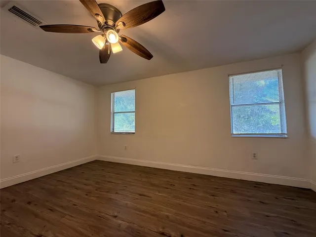 an empty room with wooden floor chandelier fan and windows