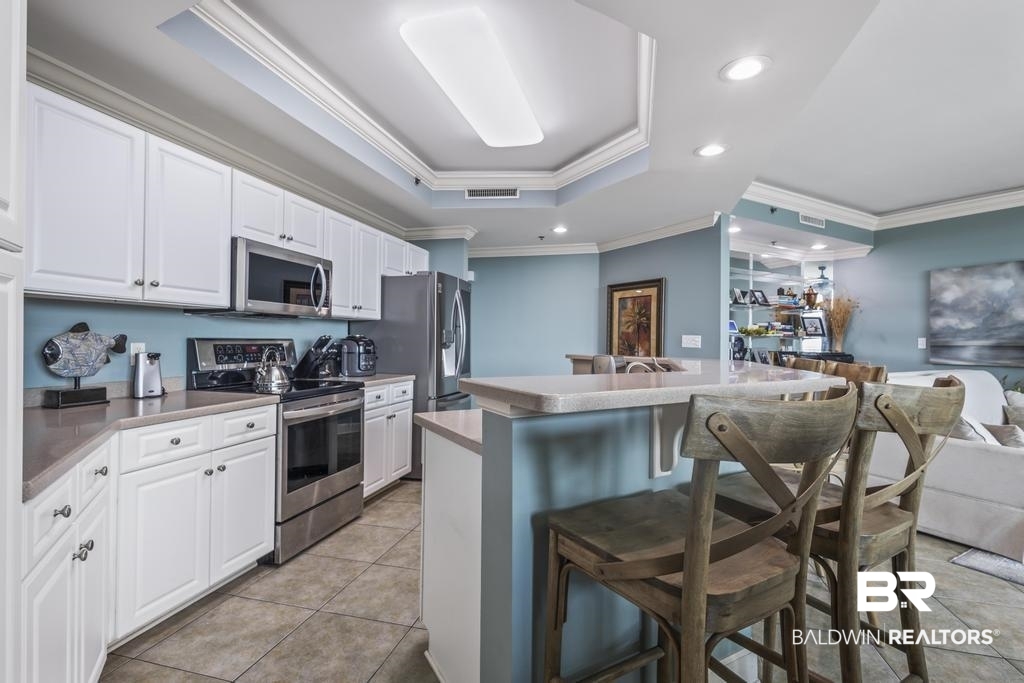 27582 Canal Road, Unit 2408 Orange Beach, AL 36561 - Photo 5 of 47 Kitchen with appliances with stainless steel finishes, a breakfast bar area, a raised ceiling, and white cabinets
