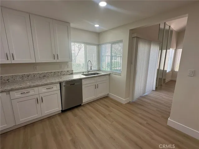 a kitchen with stainless steel appliances granite countertop a refrigerator a sink dishwasher and white cabinets with wooden floor