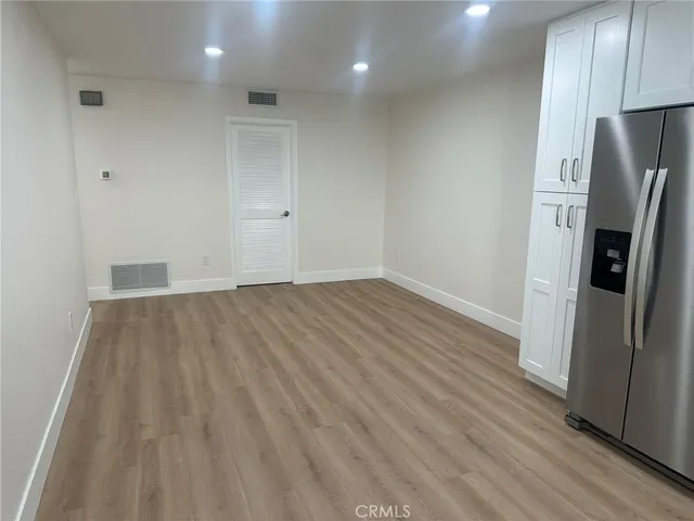 an empty room with wooden floor and a refrigerator